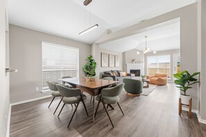 Een moderne woonkamer met een eettafel, stoelen, een bank, een open haard en een trap naar een hoger niveau.