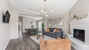 A living room with a fireplace, a sofa, a coffee table, and a television mounted on the wall. - Lake Haven Retreat - Spacious 3BR Family Escape Near Lake Lewisville (Little Elm)