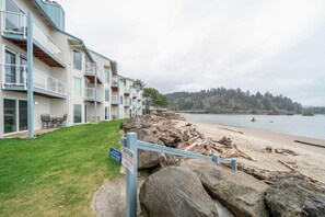 A beachfront hotel with a grassy lawn, a warning sign, and a view of the beach and forested hills. - Dock of the Bay Condo, Fireplace & Bay Views (Lincoln City)