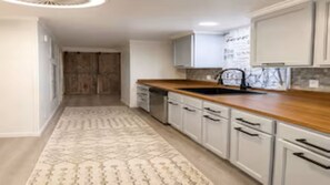 Une cuisine moderne avec des meubles blancs, un plan de travail en bois et un tapis Ă motifs.