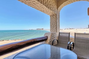 Uitzicht op het strand vanaf een beschut terras met een tafel en stoelen.