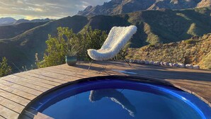 Una terraza de madera con piscina, una silla blanca y mullida, y una planta en maceta.