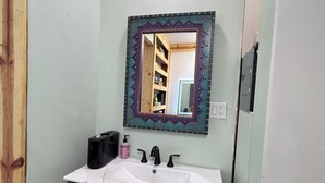 Un baño con tocador de madera, lavamanos blanco, espejo con marco decorativo e iluminación en el techo.