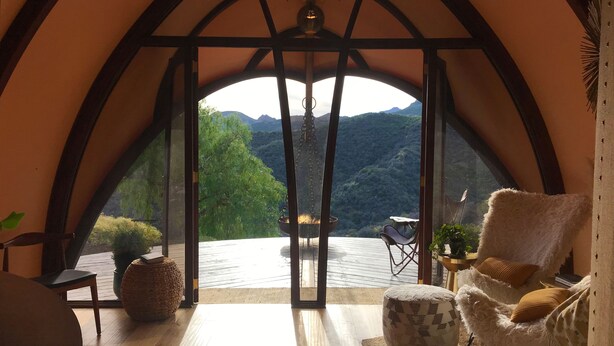 Una habitación acogedora con un amplio ventanal de arco, suelo de madera, un sillón cómodo y una pequeña mesa.