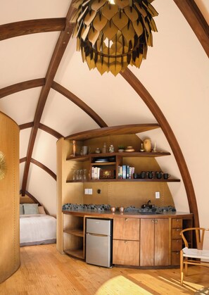 A compact kitchen with wooden beams, a built-in refrigerator, and shelves with kitchenware.