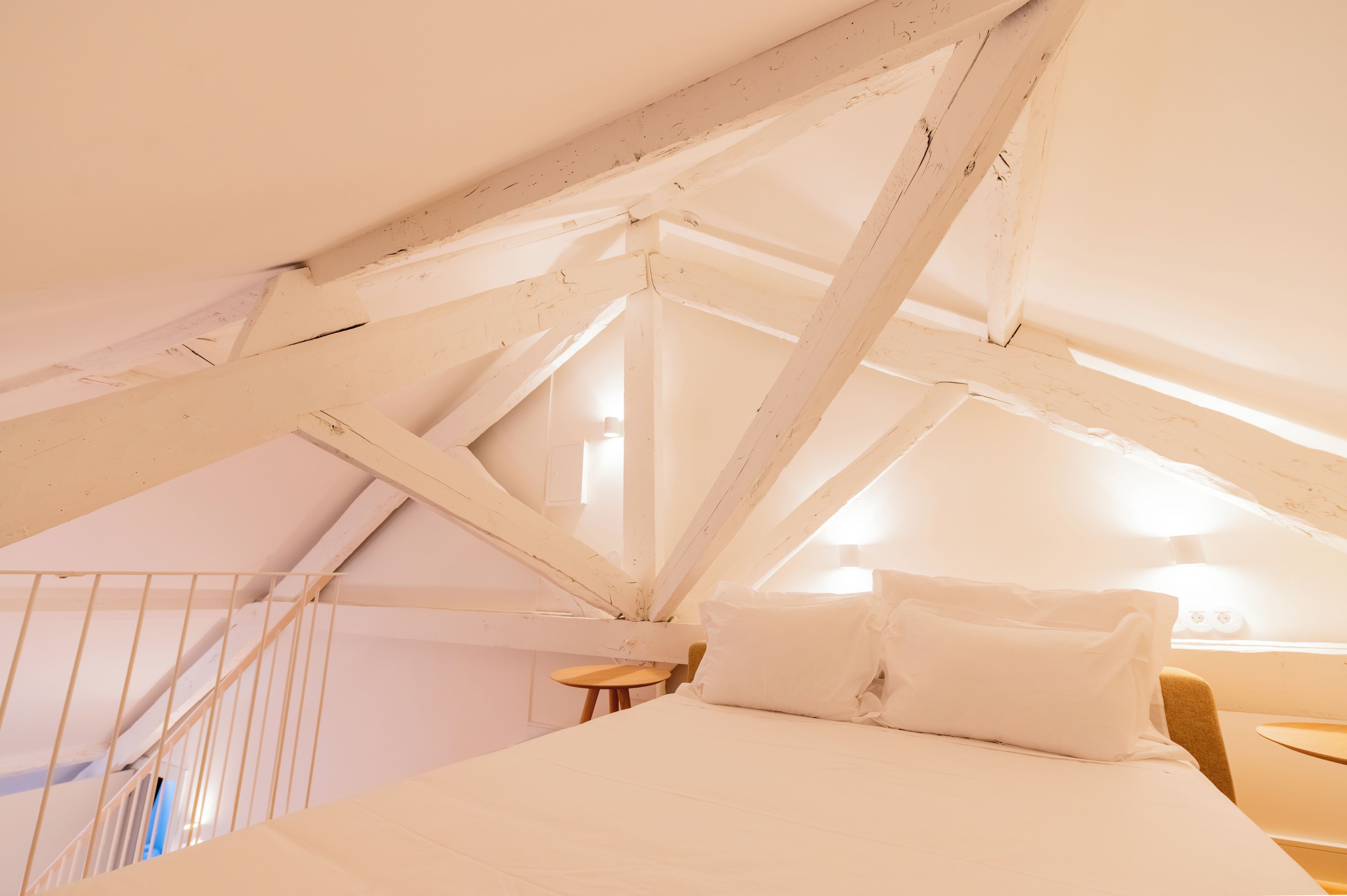 A bedroom with a sloped ceiling, a bed, a small table, and a chair.