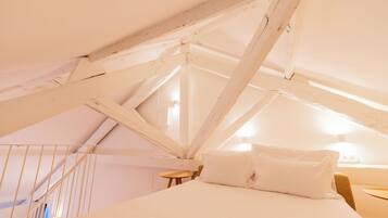 A bedroom with a sloped ceiling, a bed, a small table, and a chair.