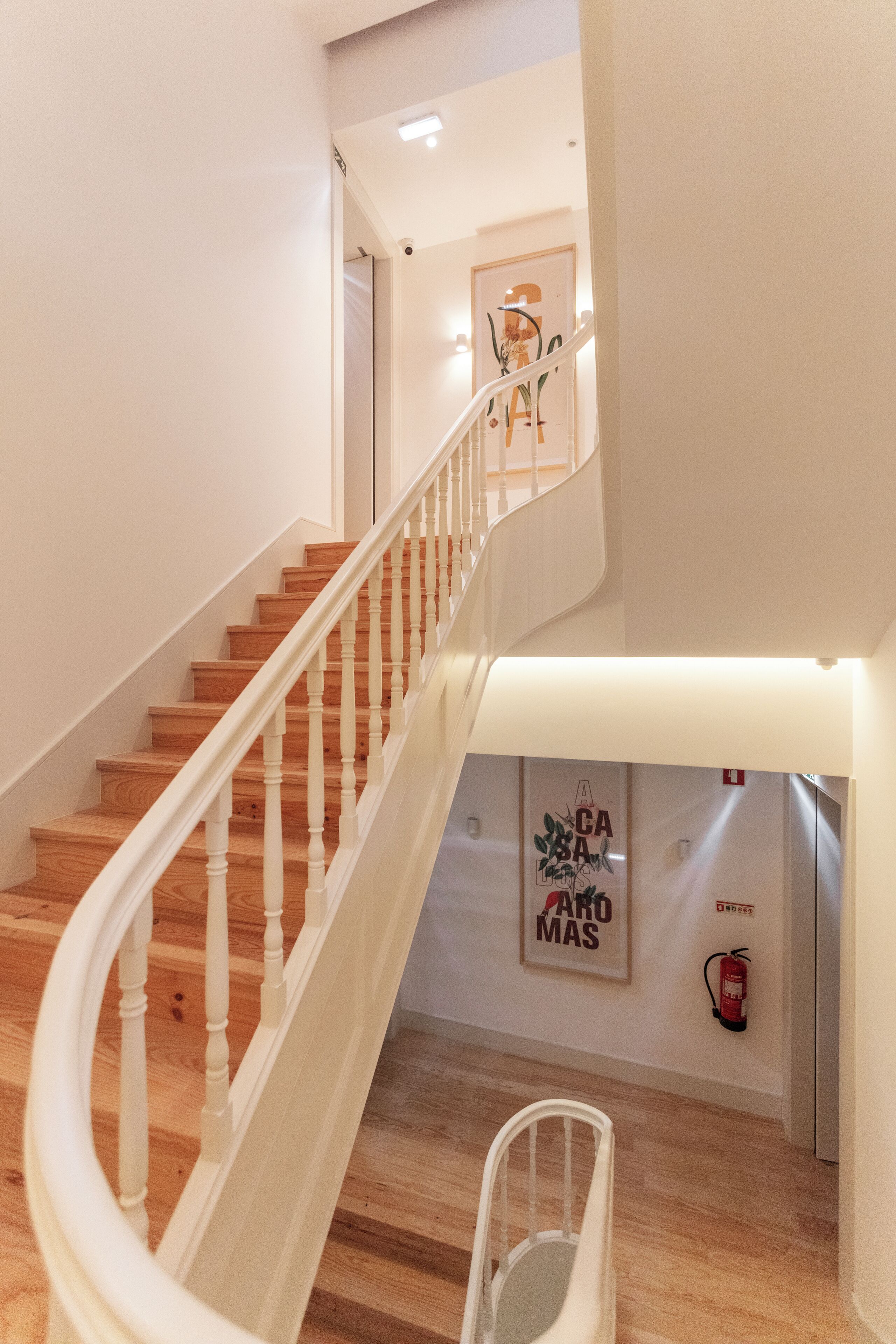 A staircase with wooden steps and white balusters, a fire extinguisher on the wall, and a framed artwork with text.