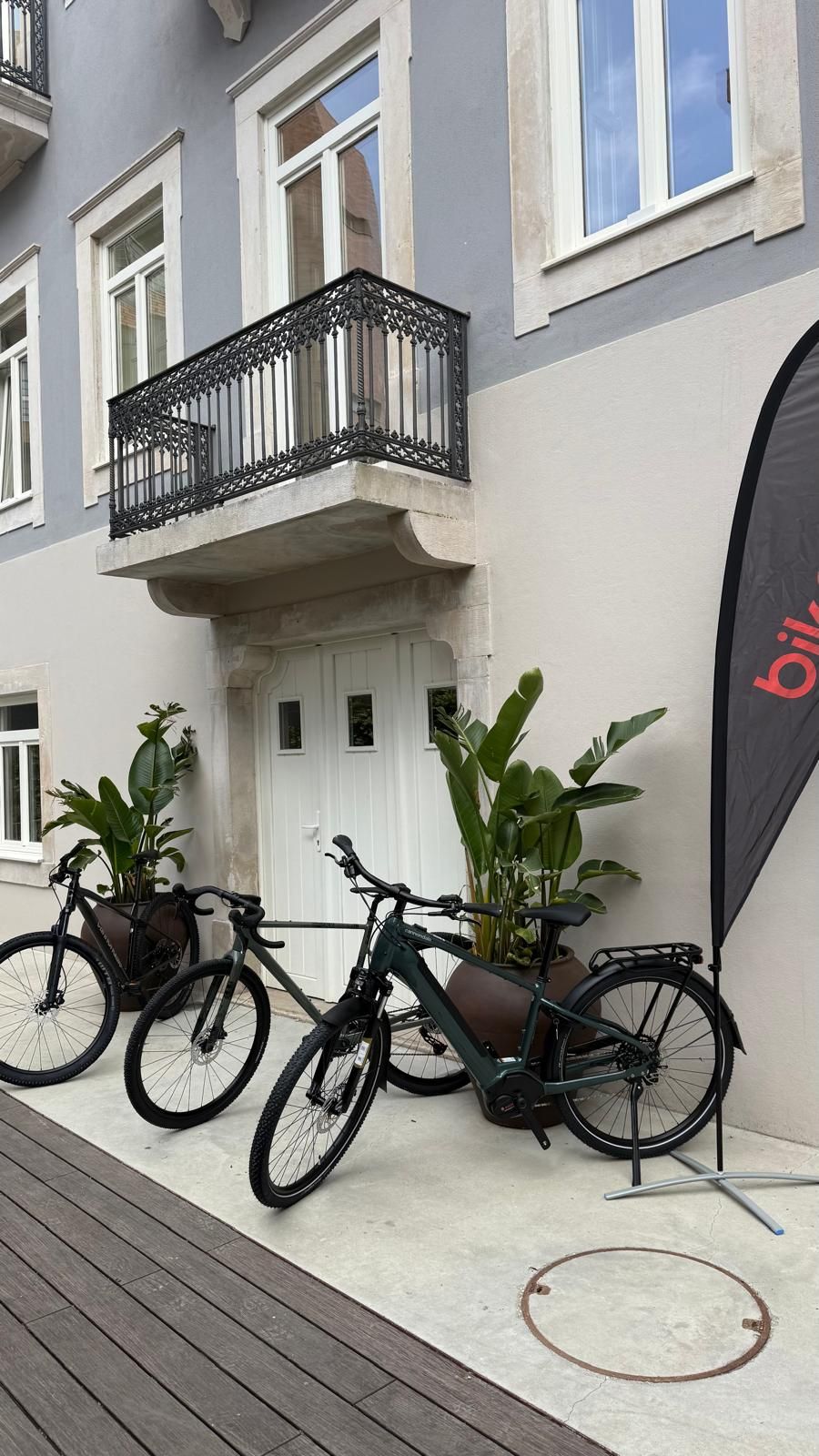 A building with a balcony, two bicycles, and potted plants.