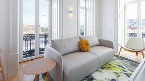 Una sala de estar moderna con un sofá gris, una mesa redonda de madera y vistas amplias por grandes ventanales.