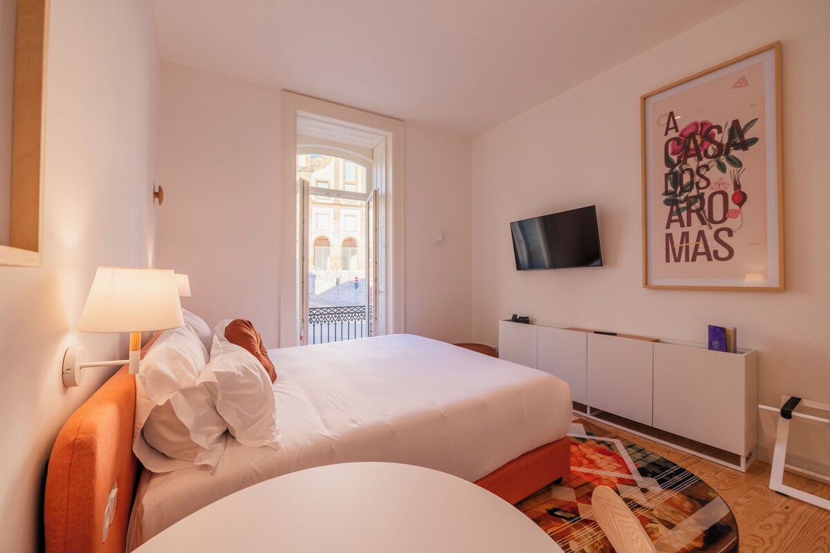 A hotel room with a bed, a television mounted on the wall, a door leading to an outdoor area, and a framed artwork on the wall.