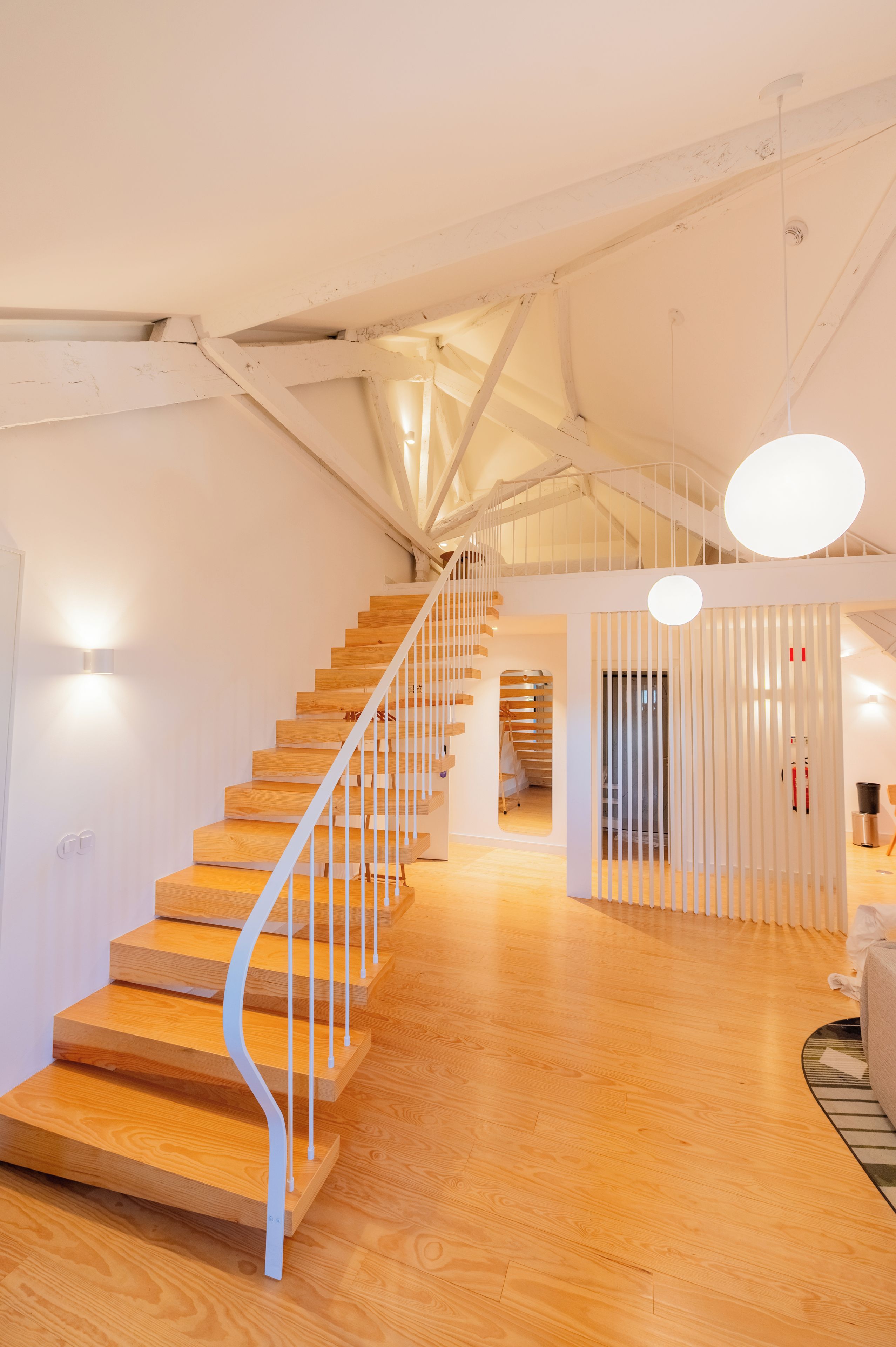 A modern interior with a wooden staircase, white walls, and a ceiling with exposed beams.