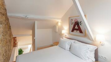 A bedroom with a bed, bedside lamps, a wall-mounted artwork, and a wooden floor.
