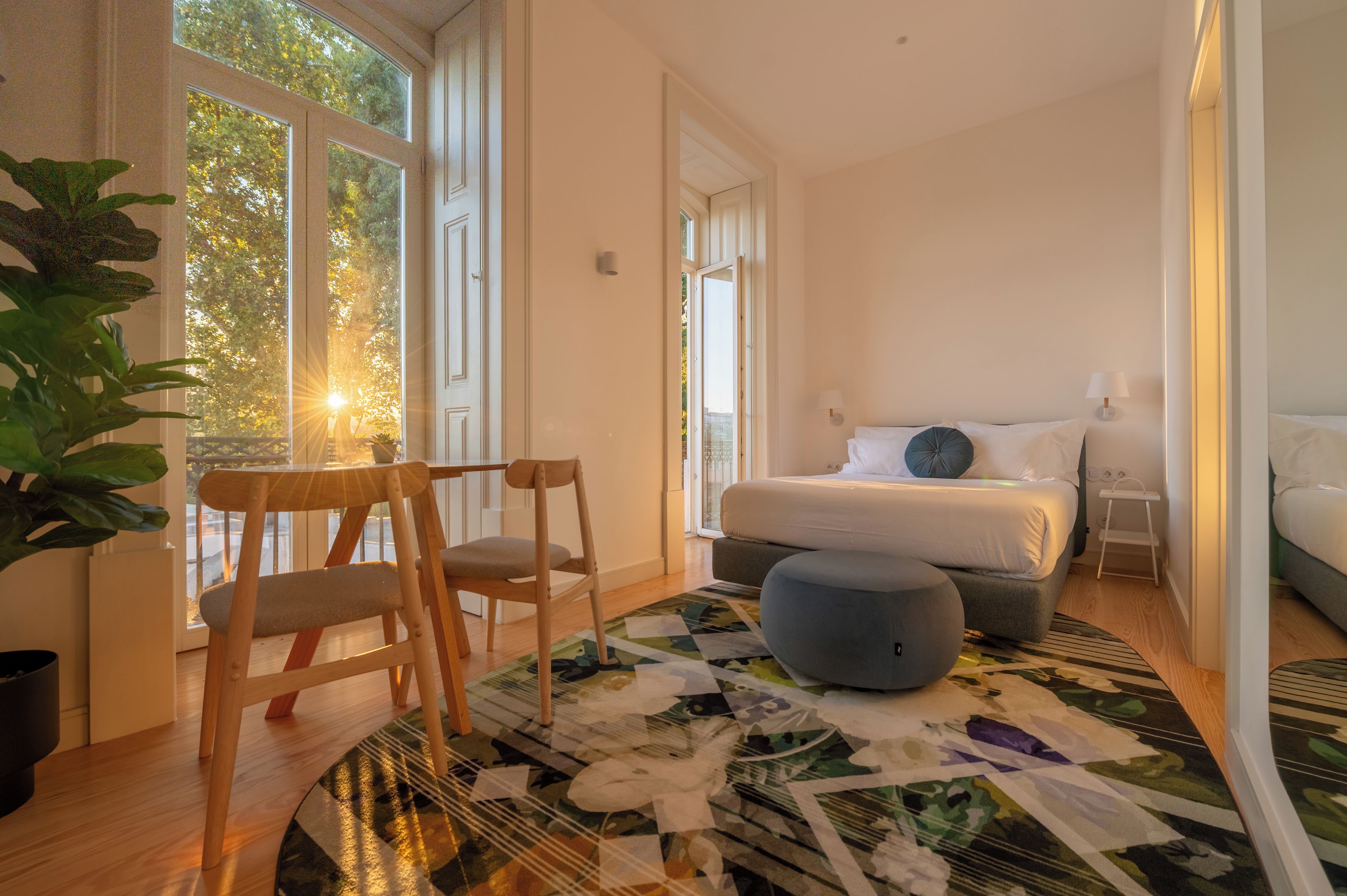 A bedroom with a bed, bedside tables, a chair, a rug, and a large window with a view of trees.