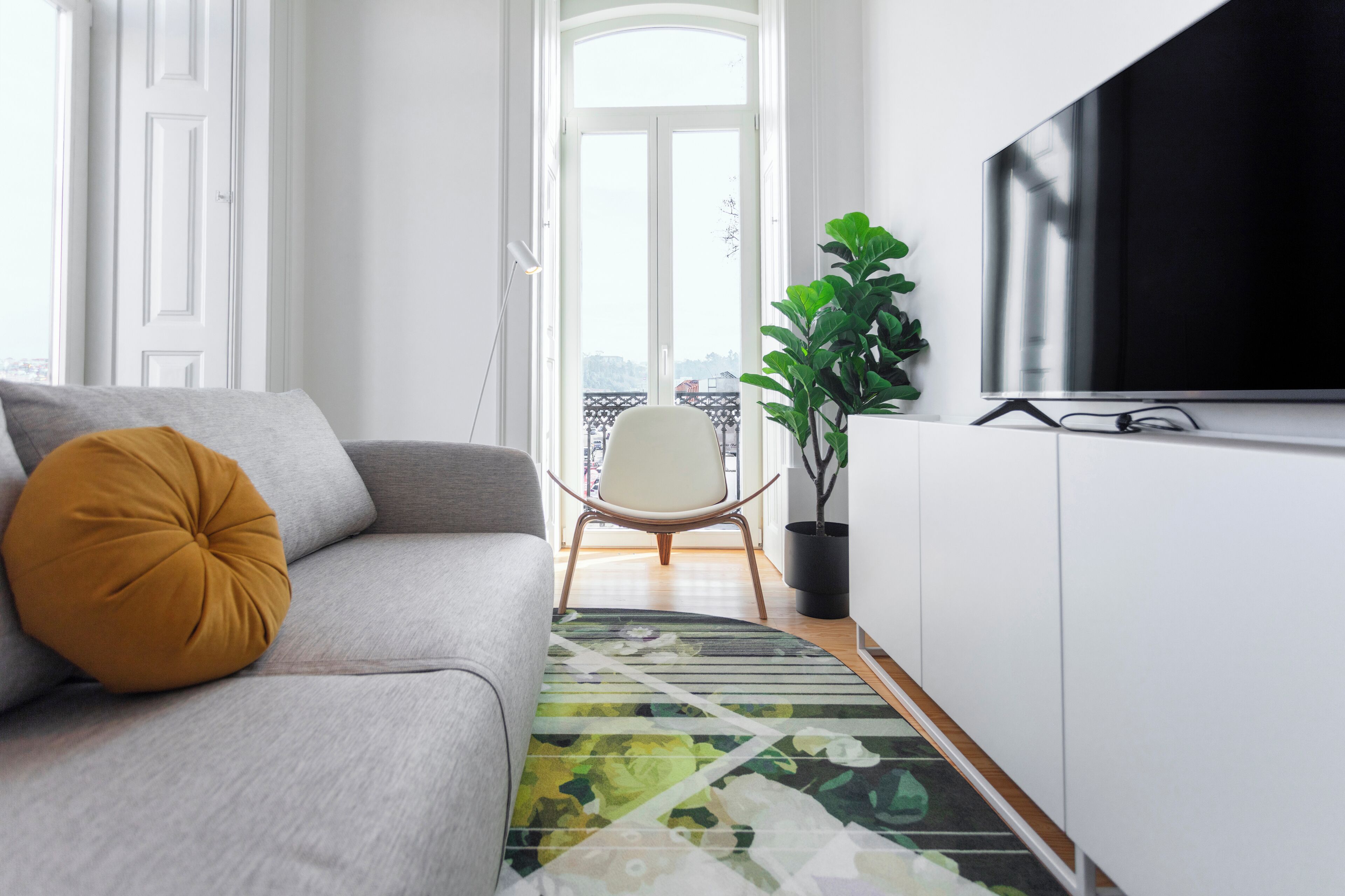 Un salon moderne avec un canapé, un téléviseur, une plante en pot et une vue dégagée sur l’extérieur grâce à une grande fenêtre.
