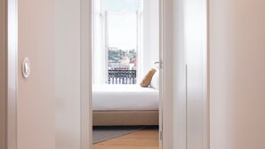 Un estrecho pasillo con suelo de madera que lleva a una habitación con cama y ventana.