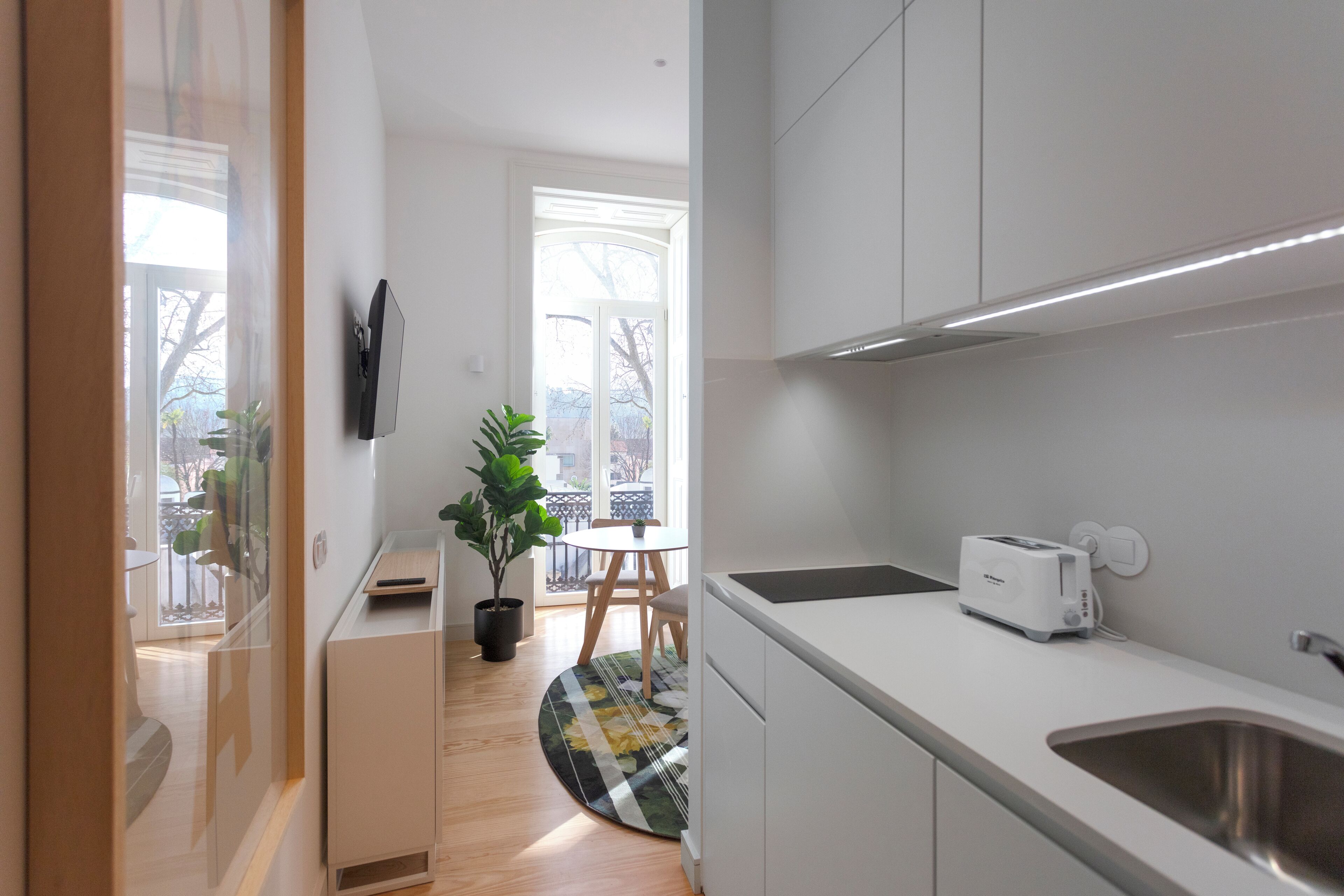 Une cuisine moderne avec des meubles blancs, un évier en acier inoxydable, un grille-pain et une plante en pot.