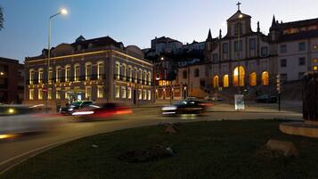 A historic building with classical architecture, a street intersection, and a grassy area with a statue.
