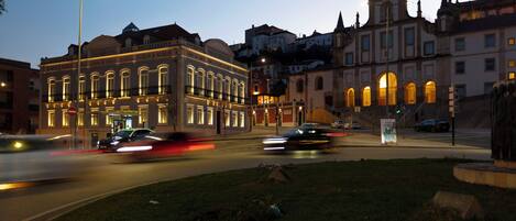 A historic building with classical architecture, a street intersection, and a grassy area with a statue.