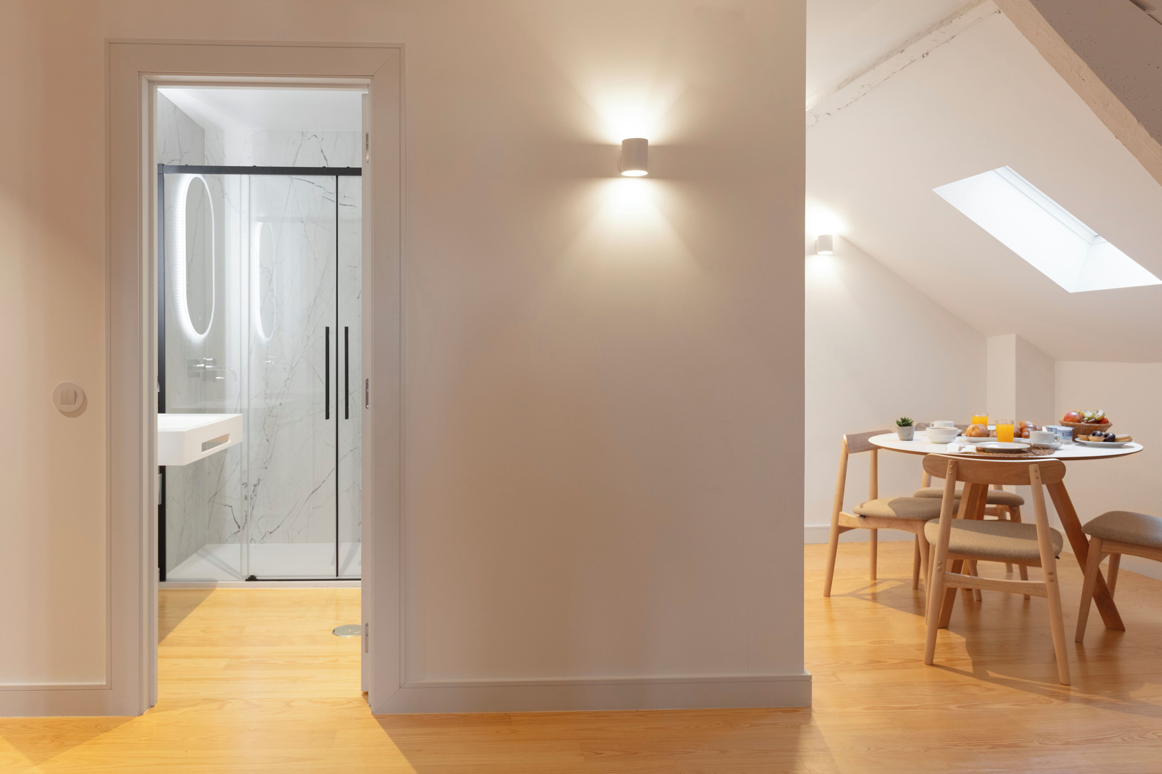 Een modern interieur met dakraam, een glazen douche en een eethoek met houten stoelen.