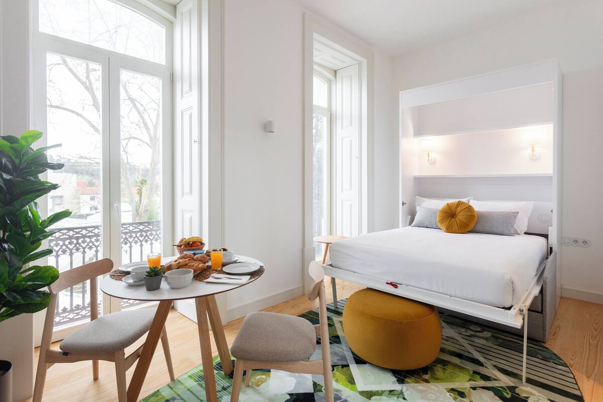 A bedroom with a bed, bedside table, chairs, and a window with a view.