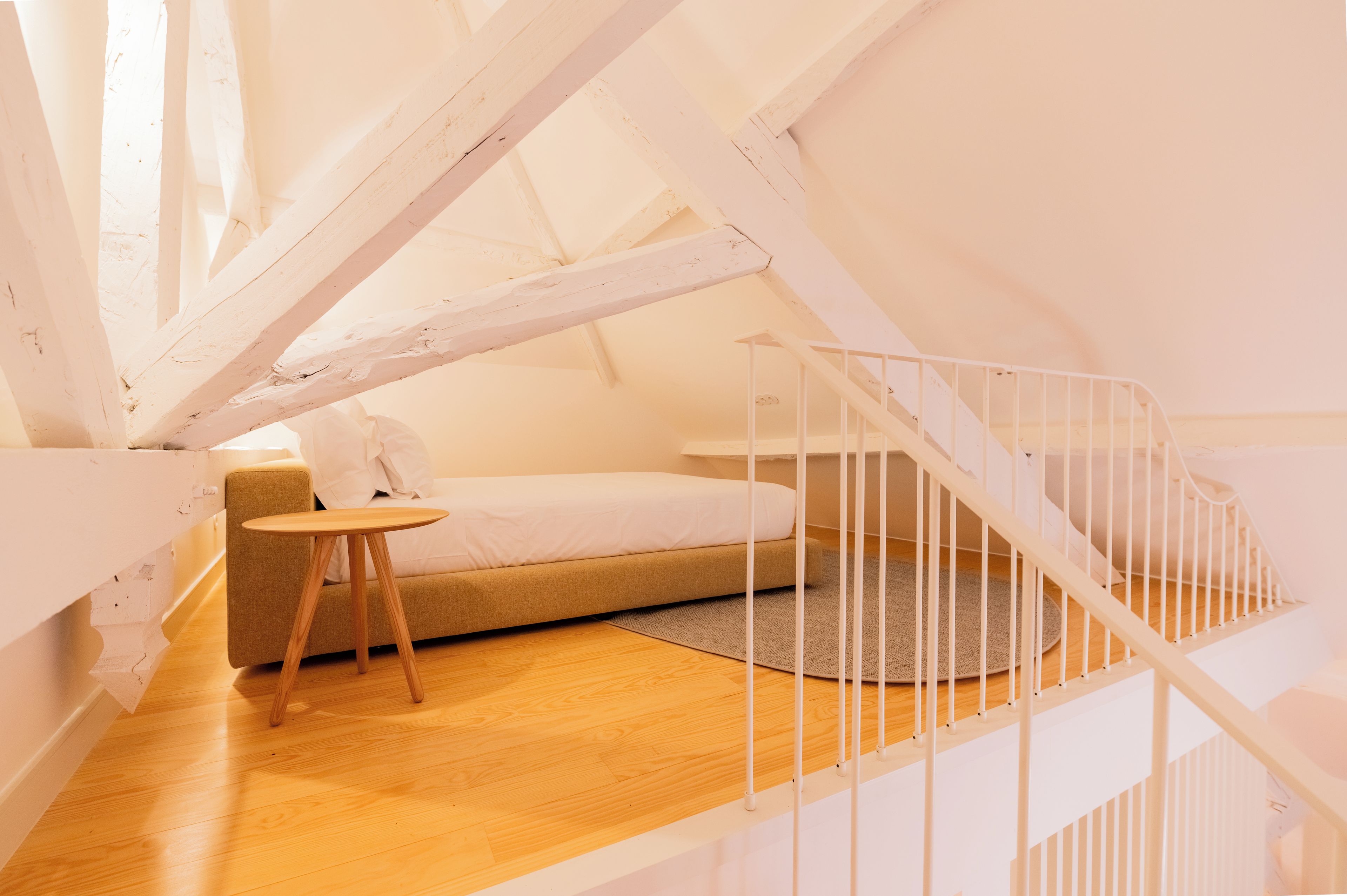 A bedroom with a bed, a small table, and a staircase.