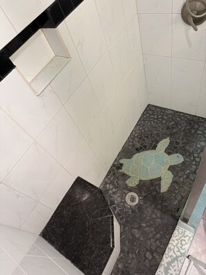 A bathroom with white tiles, a black countertop, a shower with a mosaic floor, and a towel rack. - Secluded , cozy poolside getaway.. Ocean views, near black sand beach & turtles. (Pahala)