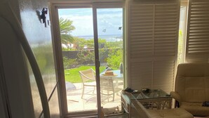 Ein Zimmer mit einer Schiebeglastür, die auf eine Terrasse führt, einem Sofa, einem Tisch und einem Kühlschrank.