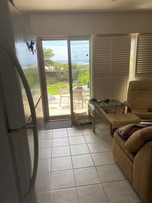 A room with a sliding glass door leading to a patio, a sofa, a table, and a refrigerator.