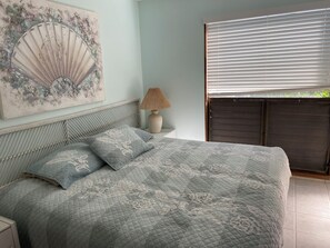 A bedroom with a bed, a bedside lamp, a wall-mounted fan, and a window with blinds. - Secluded , cozy poolside getaway.. Ocean views, near black sand beach & turtles. (Pahala)