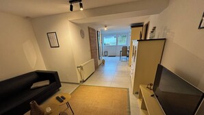 A living room with a black sofa, a wooden coffee table, a TV, and a radiator. - Vacation apartment - Cozy apartment in the Saarland (Losheim am See)