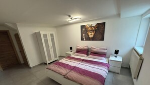 A bedroom with a bed, nightstands, a wardrobe, and a painting on the wall. - Vacation apartment - Cozy apartment in the Saarland (Losheim am See)