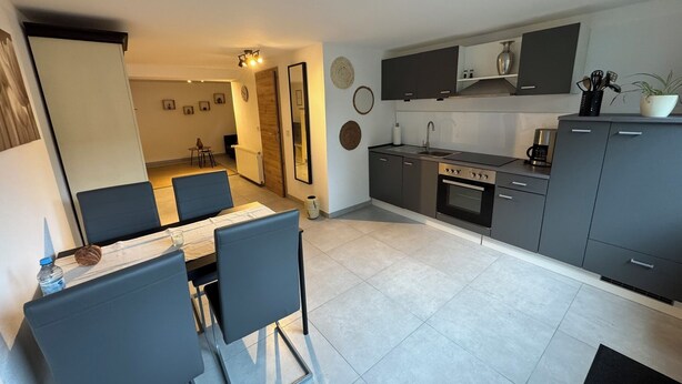 A modern kitchen with grey cabinets, a built-in oven, and a dining area with a table and chairs. - Vacation apartment - Cozy apartment in the Saarland (Losheim am See)