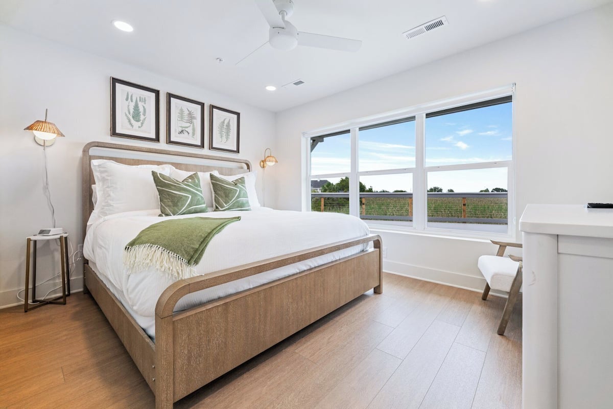 Un dormitorio con una cama, un ventanal con vistas e impresiones botánicas enmarcadas en la pared.
