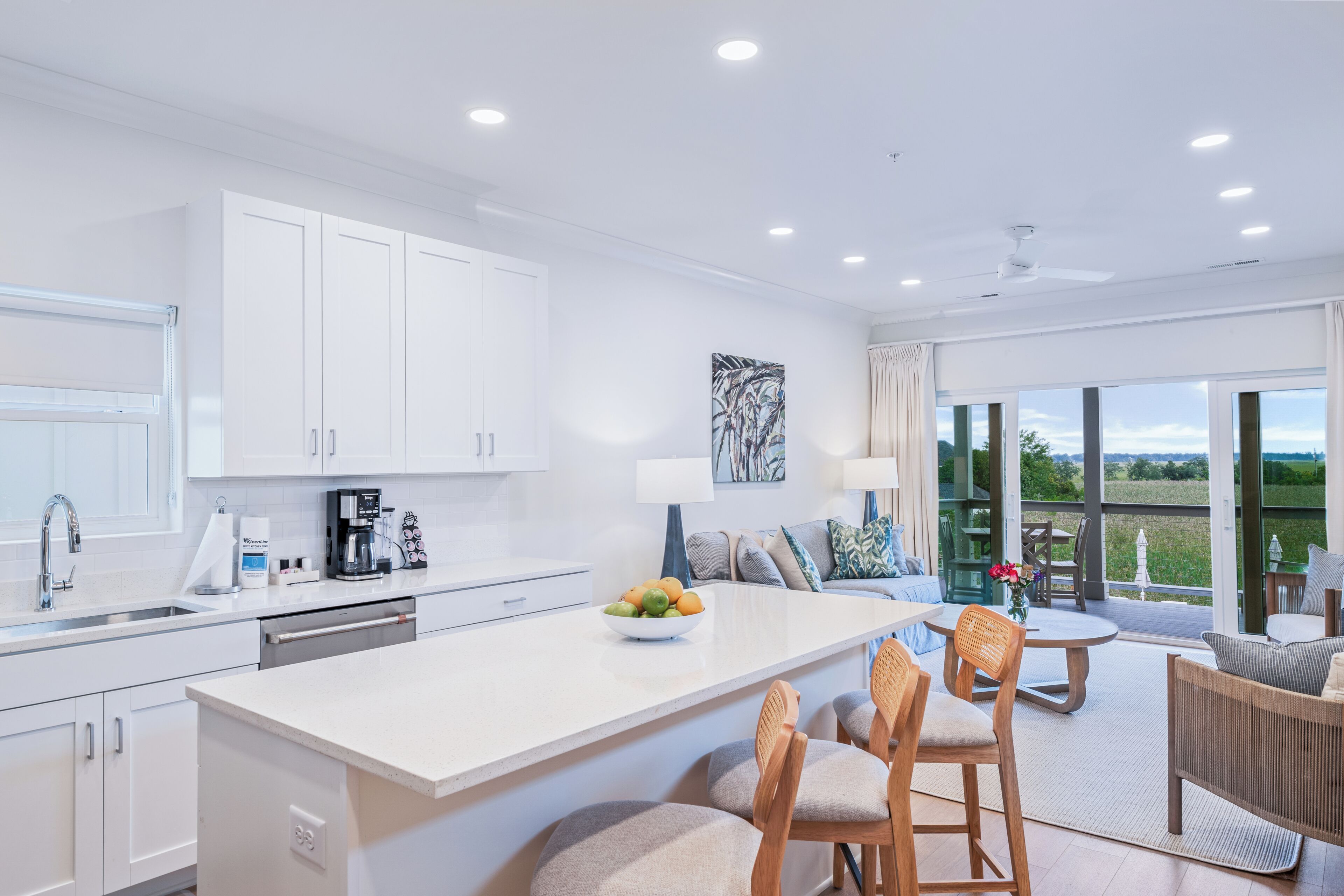 A modern kitchen with white cabinets, a central island with seating, and a dining area with a table and chairs.