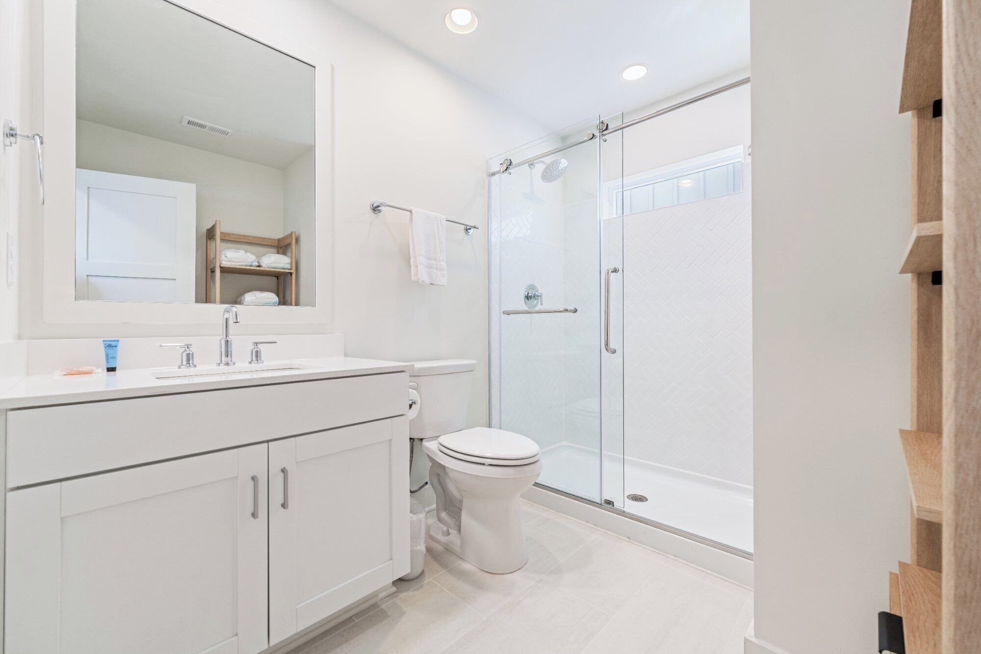 Un baño moderno con un espejo grande, tocador blanco, inodoro y zona de ducha con mampara de vidrio.