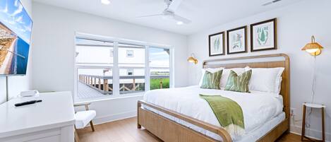A bedroom with a bed, a desk, a chair, a window, a ceiling fan, and framed pictures on the wall.
