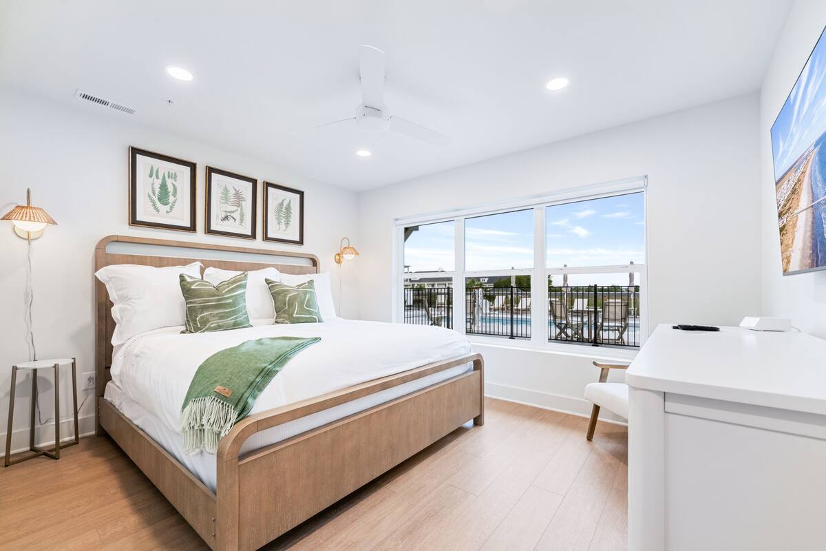 Un dormitorio con cama, escritorio, ventana con vistas e impresiones botánicas enmarcadas en la pared.