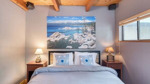 A bedroom with a bed, two nightstands, a lamp, a painting of a mountainous landscape, and a window. - Hot Tub, Shared Pier, Forest Views in Heart of Tahoma Sugar Point by Avantstay (Tahoma)