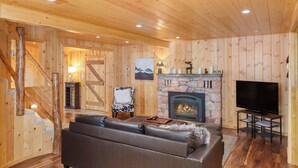 Una habitación con paneles de madera, chimenea, sofá, televisor y una escalera.