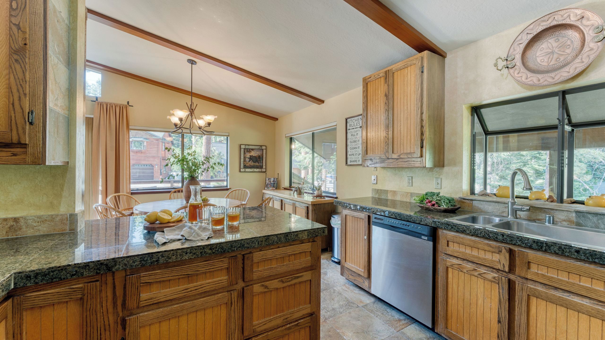 A kitchen with wooden cabinets, granite countertops, a dishwasher, and a large window.