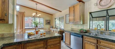 A kitchen with wooden cabinets, granite countertops, a dishwasher, and a large window.