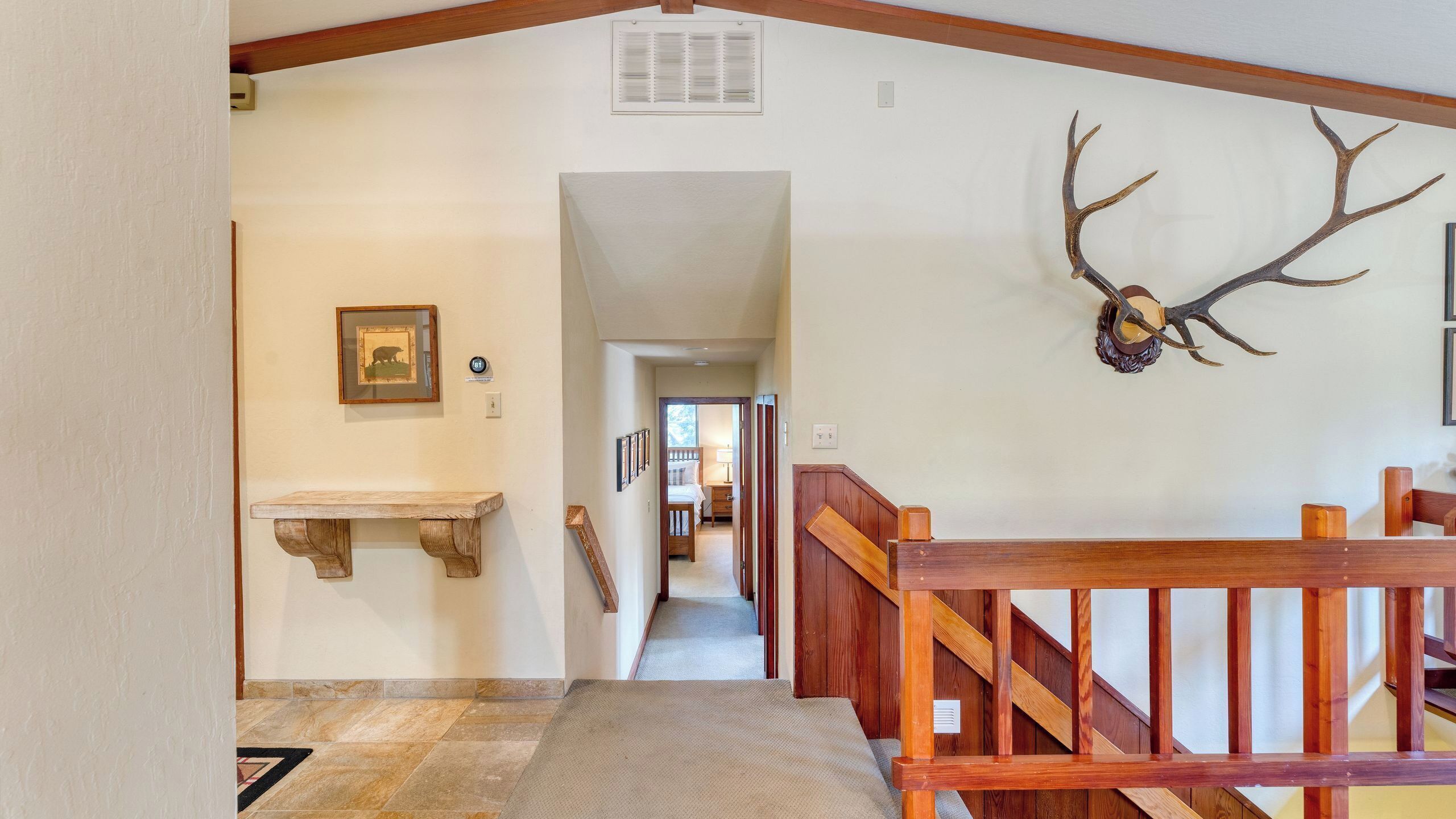 A hallway with a wooden bench, a framed picture, and a deer antler decoration.