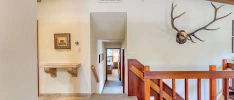 A hallway with a wooden bench, a framed picture, and a deer antler decoration.