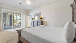 Quarto com uma cama grande, um candelabro, uma porta de correr de vidro que dá para área externa e uma cômoda com espelho.