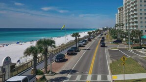 Una carretera costera con una playa a un lado, un paso de peatones y un edificio de varios pisos al fondo.