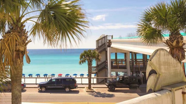 Un hotel frente a la playa con estacionamiento, vistas al océano y palmeras.