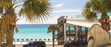 Un hotel frente a la playa con estacionamiento, vistas al océano y palmeras.