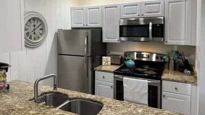 A kitchen with white cabinets, stainless steel appliances, a granite countertop, and a wall clock. - Charming condo, with shared pool, Gym, and Tennis (Miramar Beach)