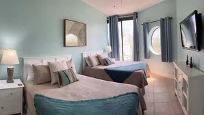 A hotel room with two beds, a TV, a window with curtains, and a lamp. - Charming condo, with shared pool, Gym, and Tennis (Miramar Beach)